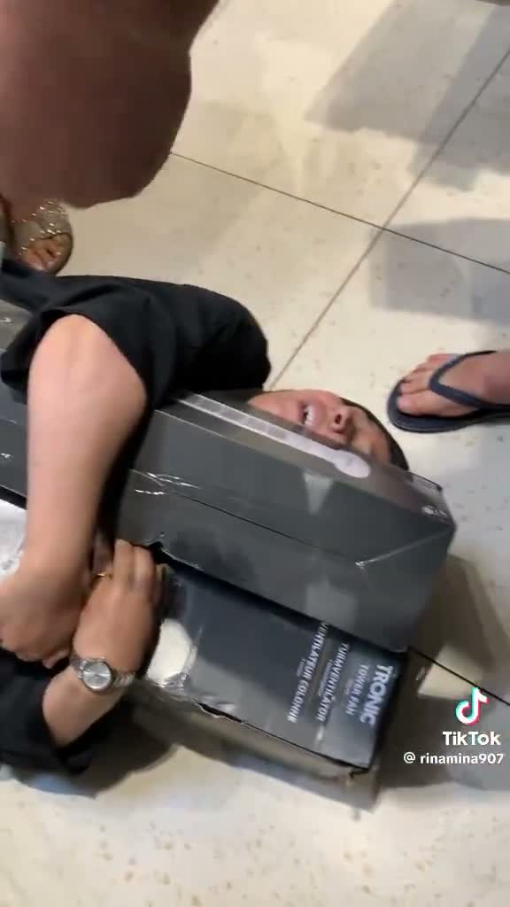 Une personne est allongée par terre, tenant des paquets de produits tout en souriant, illustrant le moment humoristique du jeu vidéo à travers un loot sécurisé.