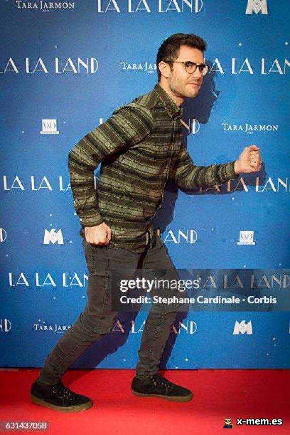 Darren Criss avance d’un pas pressé sur un tapis rouge devant un photocall de La La Land, utilisé pour évoquer une fuite gênée.